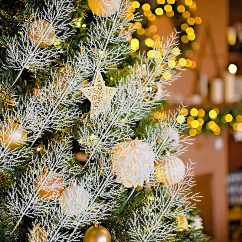 Close-up of white artificial pine branch tucked into a lit Christmas tree